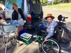 A LevelUp worker is assisting a gentleman in a wheelchair to experience camping from his vehicle.