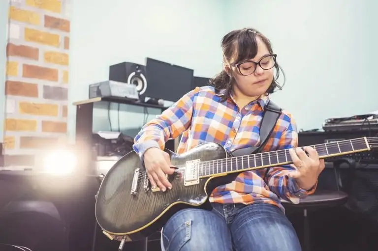 LevelUp provides a SIL for a woman wearing eyeglasses, sitting, and playing the guitar with skill and passion.