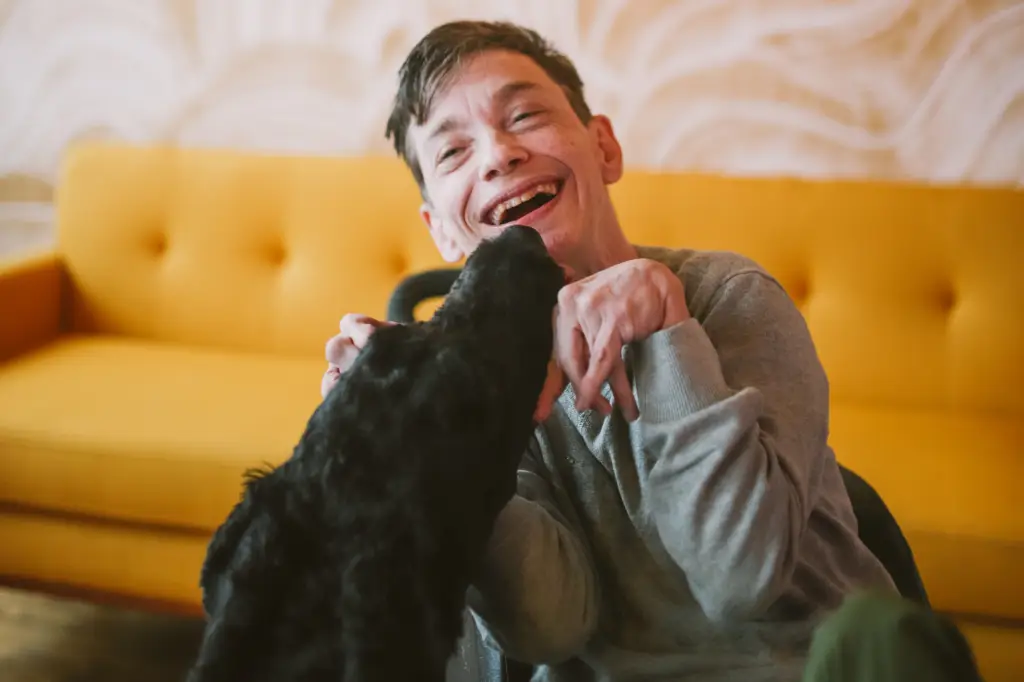 A man in a wheelchair happily pets a dog, showing the LevelUp high-intensive support.