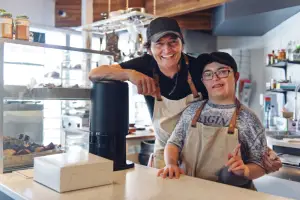 Two people wearing barista outfits behind the café counter demonstrate how LevelUp helps empower people with disabilities.